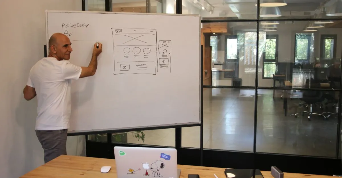 A designer sketching a website wireframe on a whiteboard, with the hero area blocked out at the top of the layout.