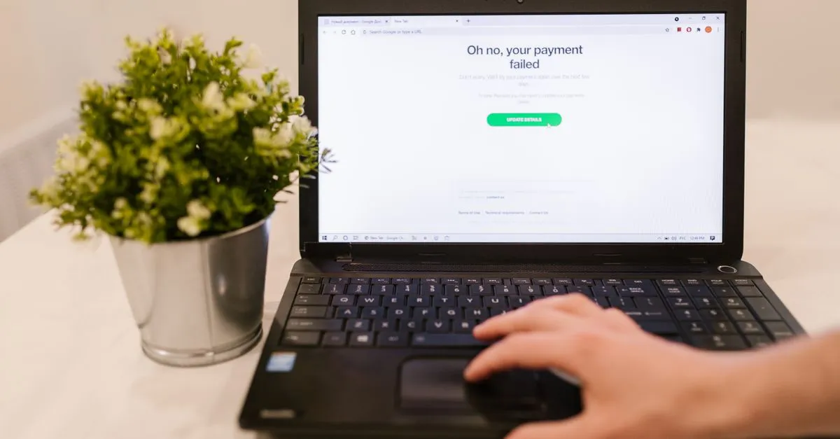 A laptop on a desk showing a browser error page that reads "Oh no, your payment failed," next to a small potted plant.