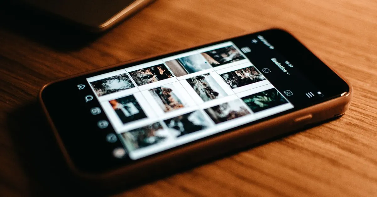 A smartphone resting on a wooden desk showing a grid of image thumbnails, standing in for a scrollable mobile content feed.