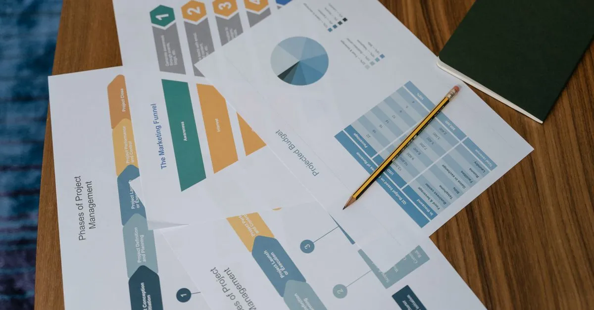 Printed marketing funnel, project phases, and projected budget charts spread across a wooden desk.