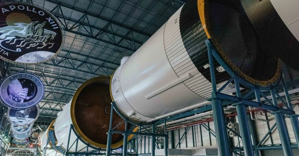 A Saturn V rocket displayed horizontally beneath Apollo mission emblems in a space museum, the launch vehicle that made Huntsville the Rocket City.