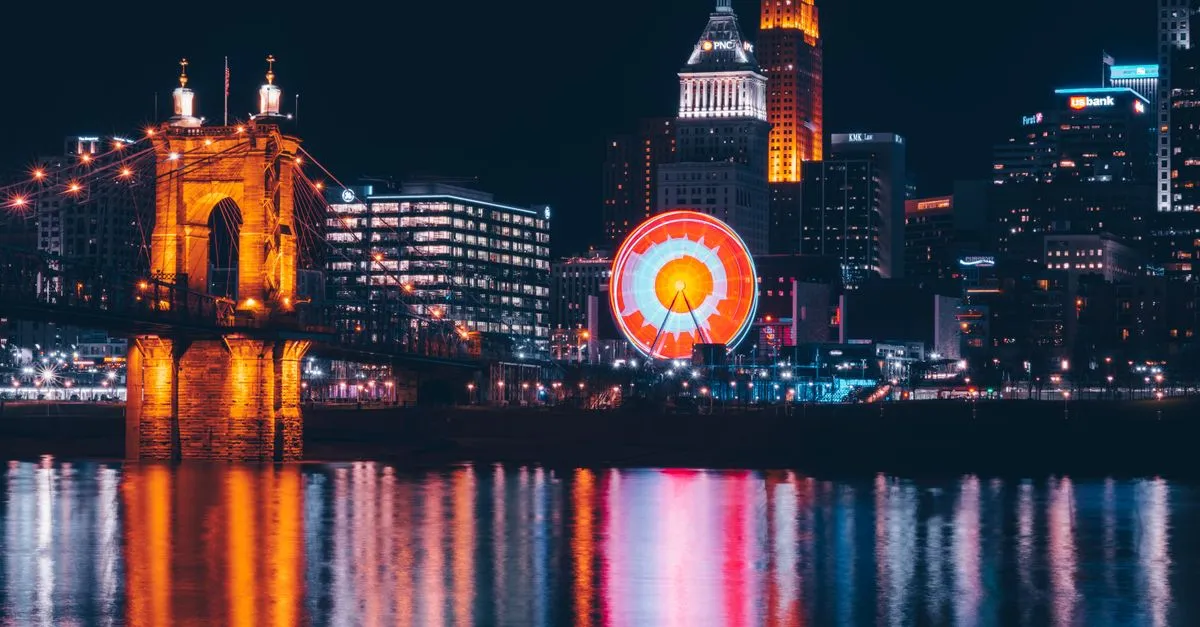 The Cincinnati skyline lit up at night behind the Roebling Suspension Bridge and the Smale Riverfront ferris wheel, the downtown market where the map pack is won.