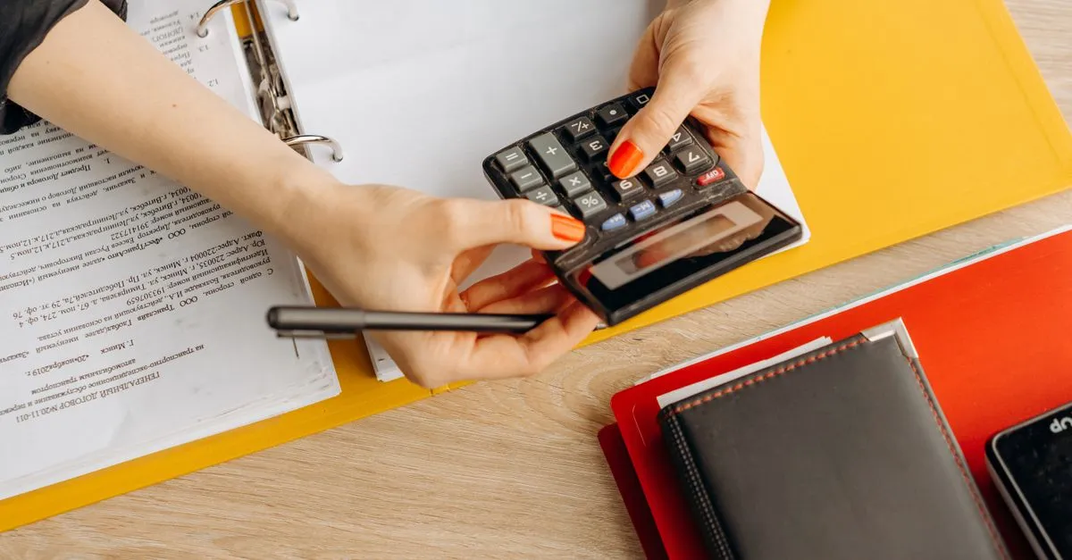 An accountant using a calculator at a desk covered with tax documents and folders.