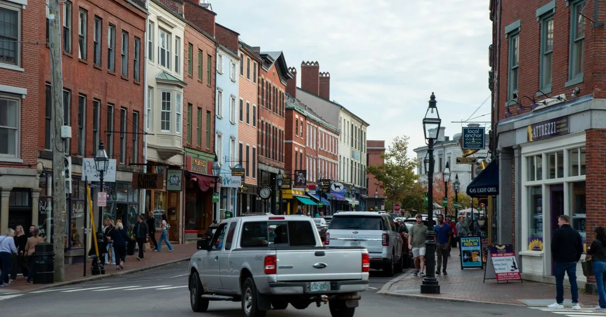A busy downtown street lined with brick storefronts and pedestrians under an overcast sky.