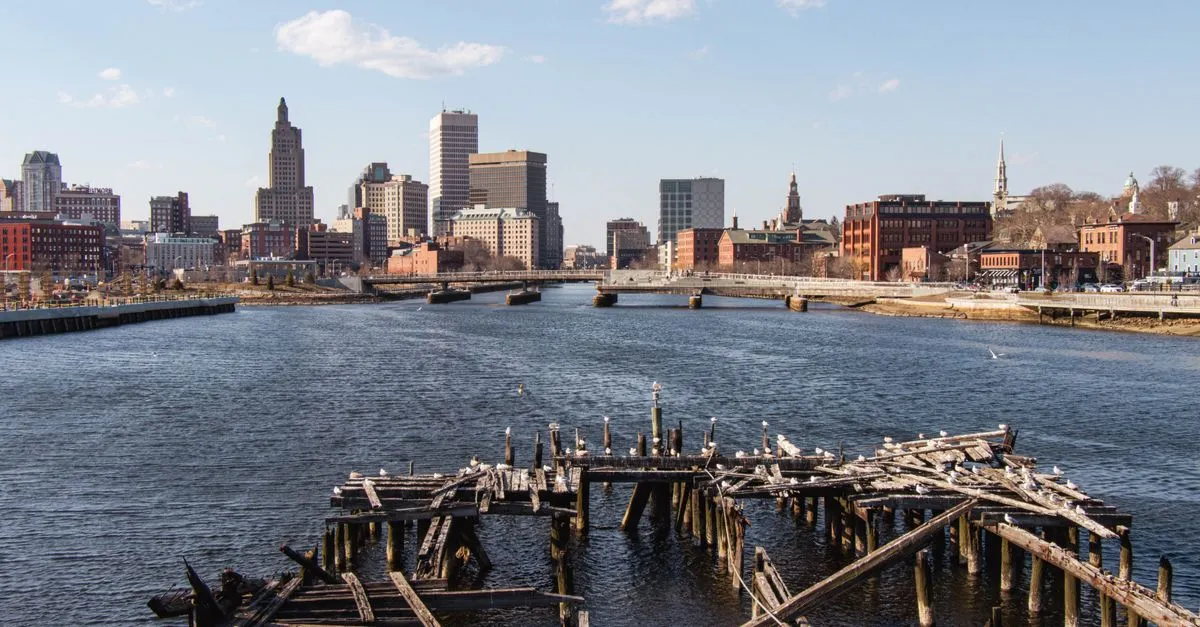 The downtown Providence, Rhode Island skyline and the Industrial Trust tower rising above the river, seen past an old wooden dock on a clear day.