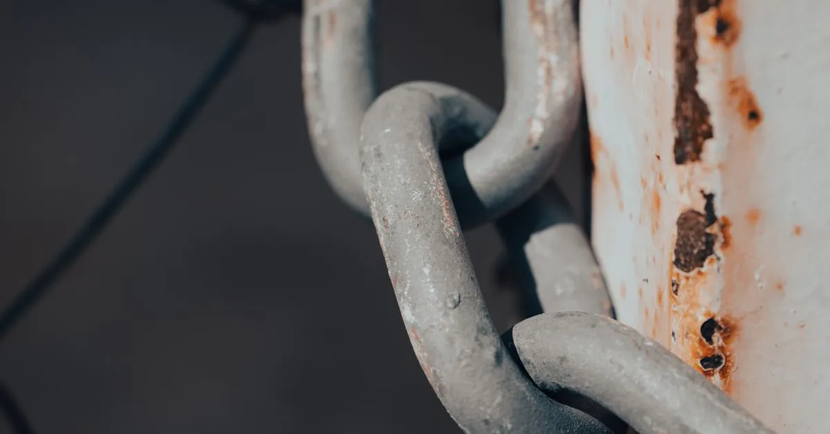 Close-up of a rusty metal chain wrapped around a weathered, rust-stained post, standing in for a broken link.