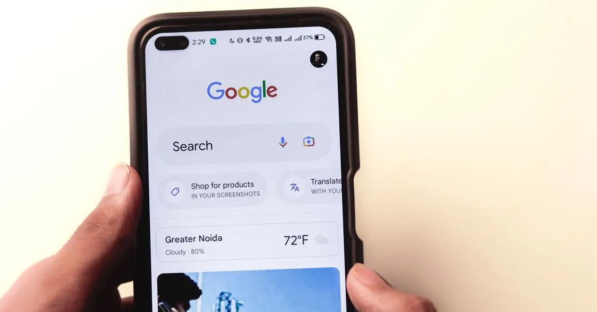 A hand holding a smartphone showing the Google search screen, the surface where a knowledge panel appears.