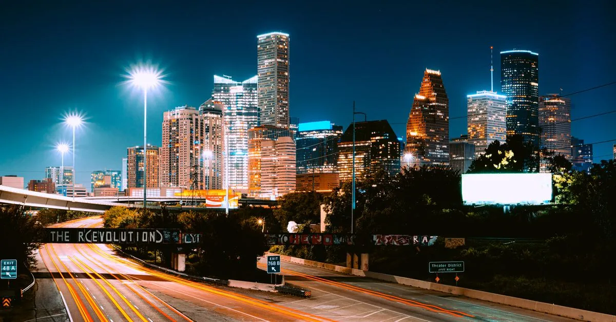 Downtown Houston skyline lit up at night with light trails on the freeway below and a Theater District sign, the sprawling metro where the map pack is won.