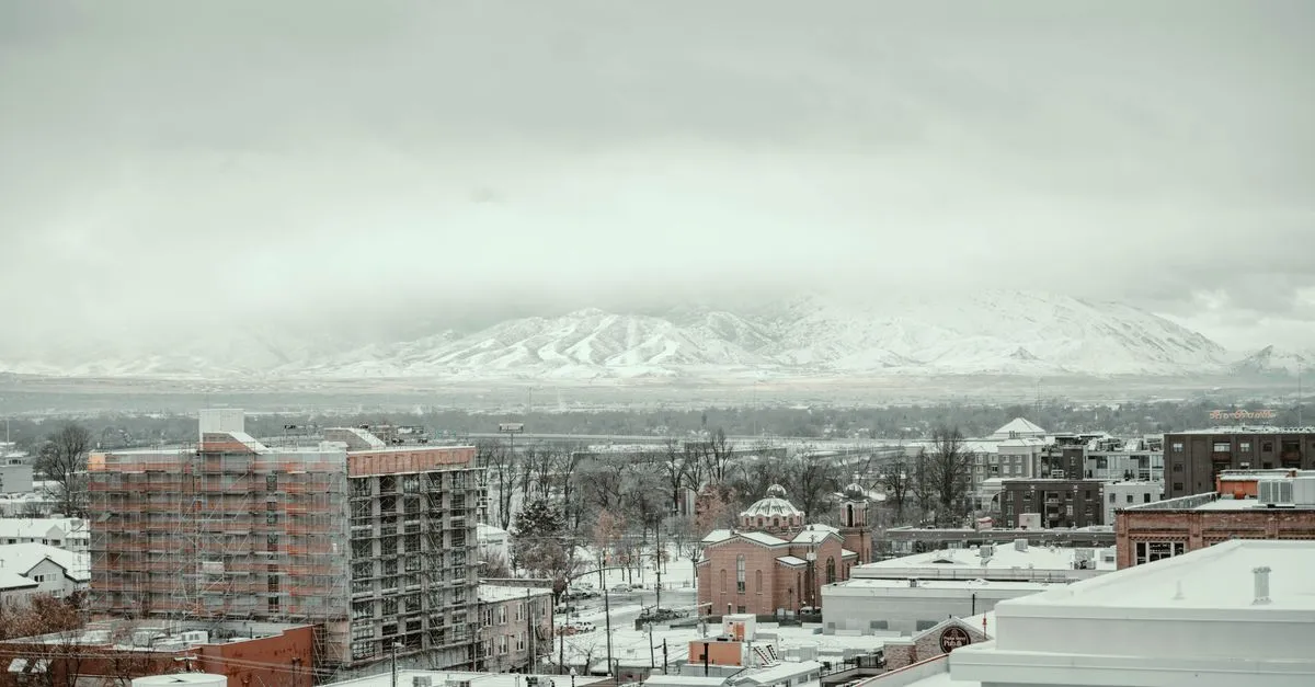 A winter cityscape of Salt Lake City with snow-covered downtown buildings and the Wasatch Range rising behind them.