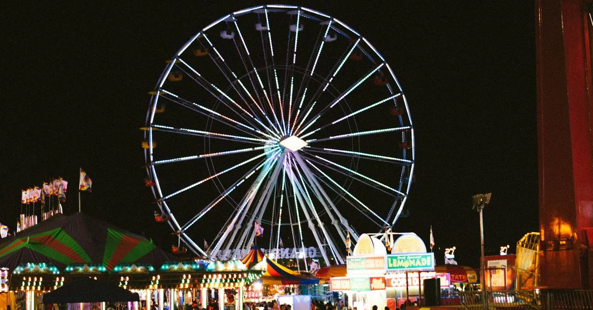 A glowing Ferris wheel lit up at night above carnival food stands at a summer fair in Des Moines, Iowa.