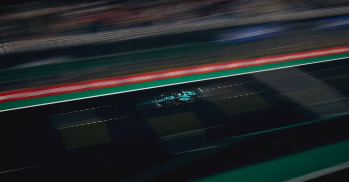A blue Formula-style race car blurred with motion as it streaks along a dark track at night, red and green edge lines smearing into speed.