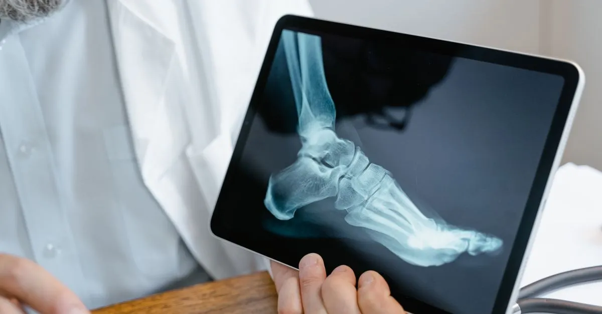 An orthopedic doctor holding a tablet that shows a foot and ankle x-ray during an exam.