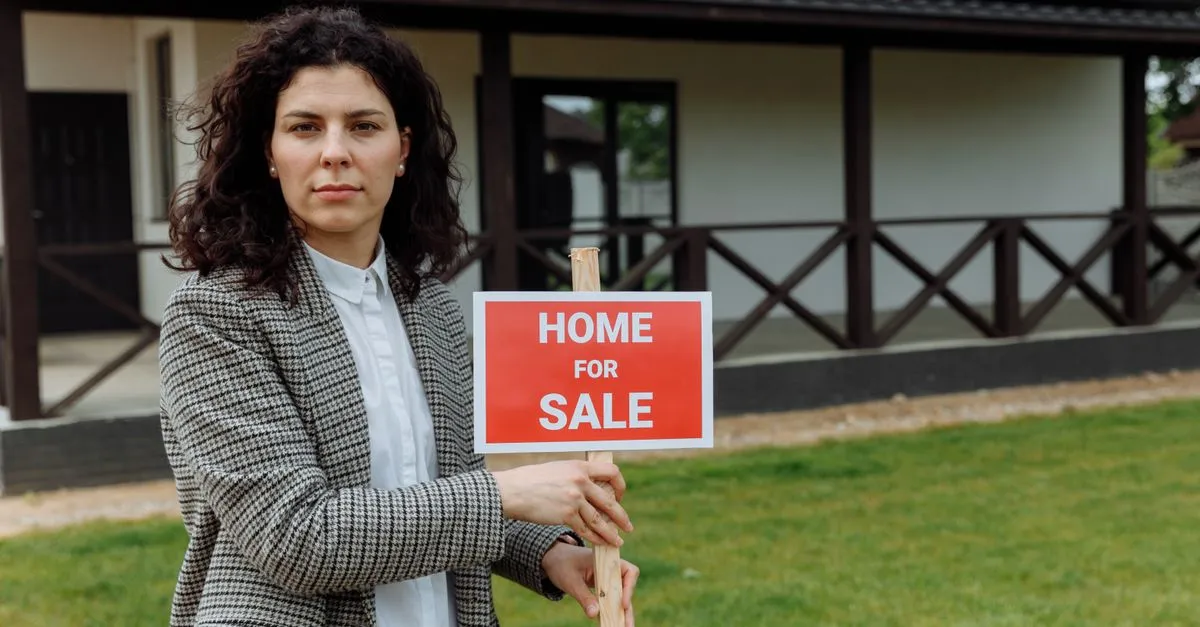 A real estate agent holding a sign outside a house, the kind of business websites for realtors are built to promote.