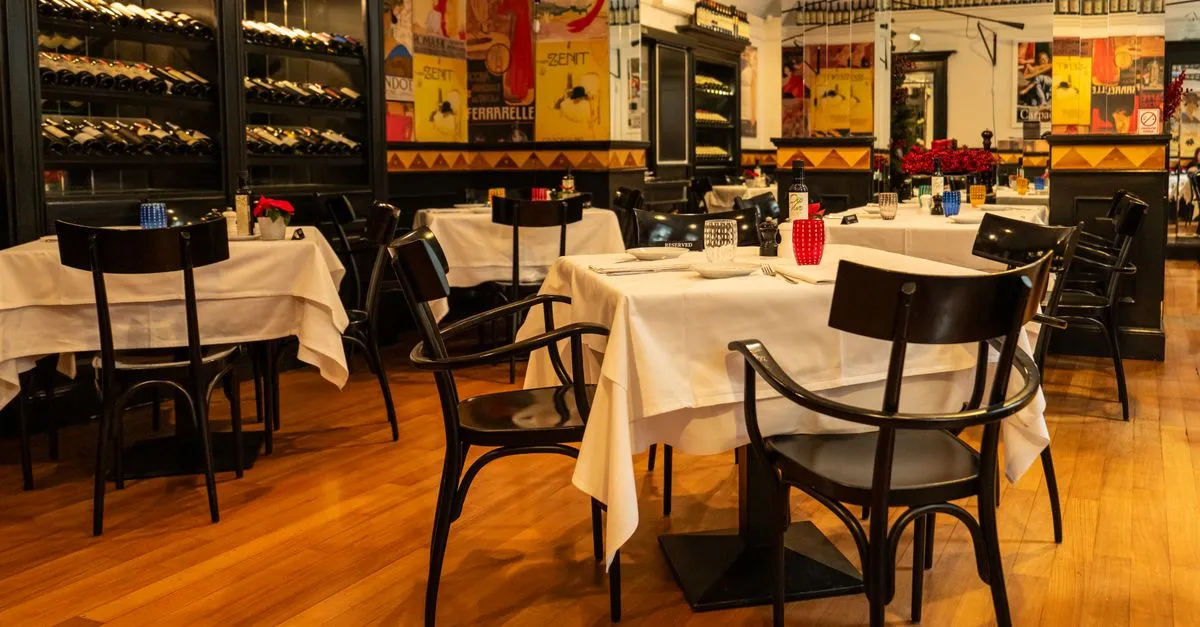 An elegant restaurant dining room with white-clothed set tables and a wine display, the kind of room a restaurant website should sell.