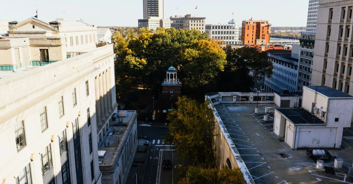 An elevated view of a downtown Richmond, Virginia street lined with historic stone buildings, a church bell tower, and autumn trees, with a rooftop parking deck to the right.