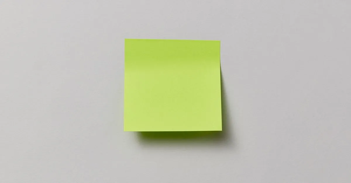 A single blank green sticky note on a plain grey wall, surrounded by empty space.