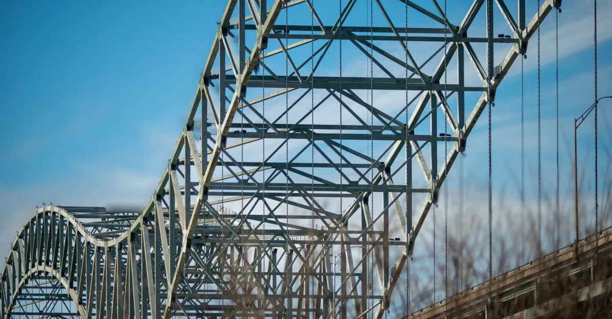 The steel truss arches of the Hernando de Soto Bridge spanning the Mississippi River into Memphis, Tennessee, under a clear blue sky.