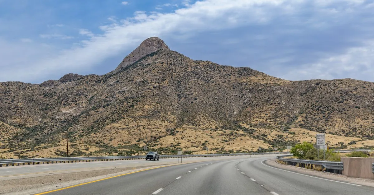 A desert highway curving toward rugged mountains under a wide sky in the arid landscape around El Paso, Texas.