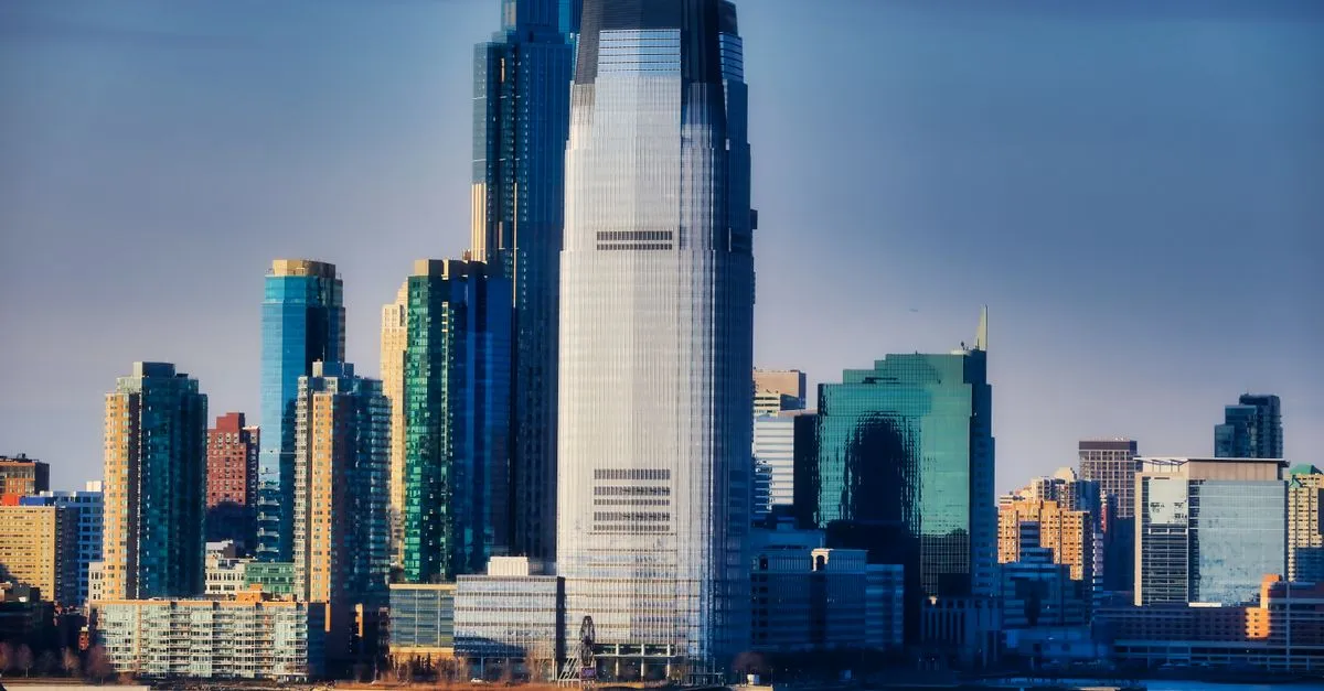 The Jersey City waterfront skyline at Exchange Place, with the tall Goldman Sachs Tower rising above glass high-rises along the Hudson River.