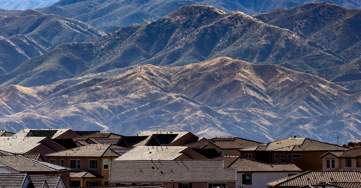 Tile-roofed homes in a master-planned desert community beneath a large arid mountain range.