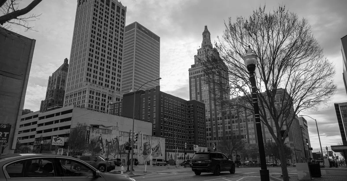 A black and white photo of downtown Tulsa, Oklahoma, its high-rise towers and a historic art deco skyscraper rising over a quiet street.