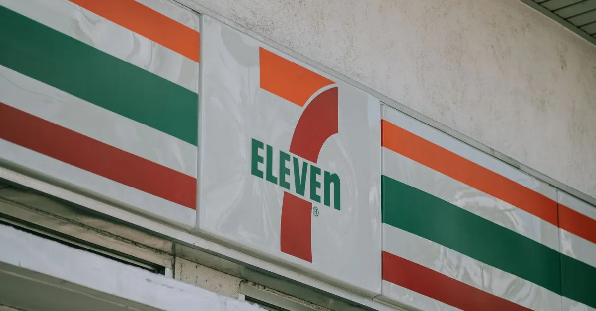 Close-up of a franchise convenience store sign lit above the entrance of a local storefront.