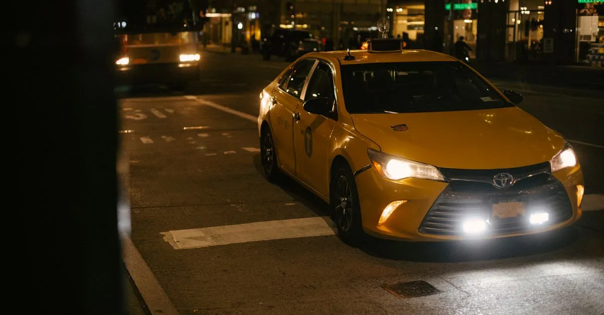 Yellow taxi cab driving down a busy city street at night with headlights glowing in traffic.