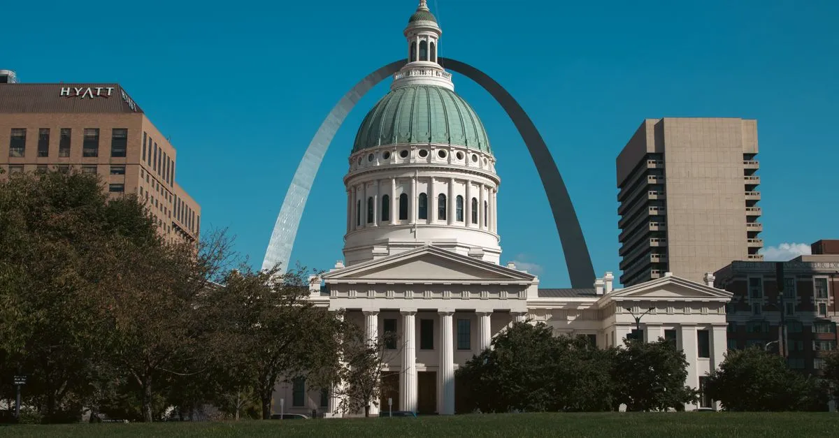 The historic Old Courthouse in downtown St. Louis framed by the Gateway Arch under a clear blue sky.