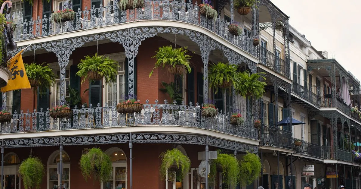 Wrought iron balconies draped in ferns and flowers on a red-brick building in the New Orleans French Quarter.