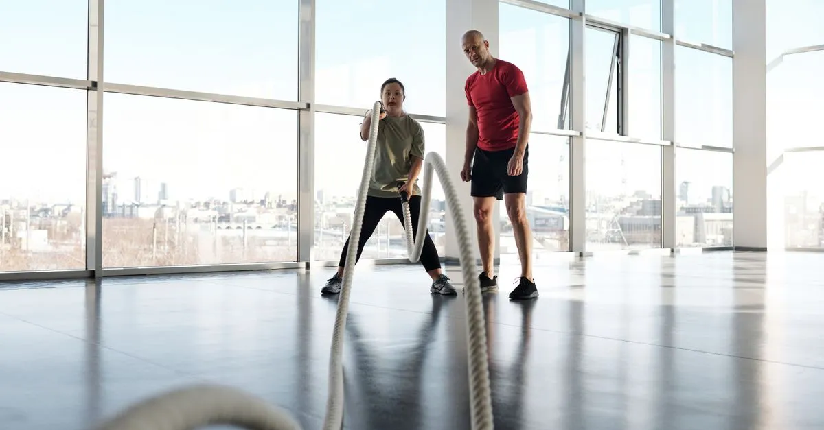 A trainer coaching a member through a battle-ropes workout in a modern gym.