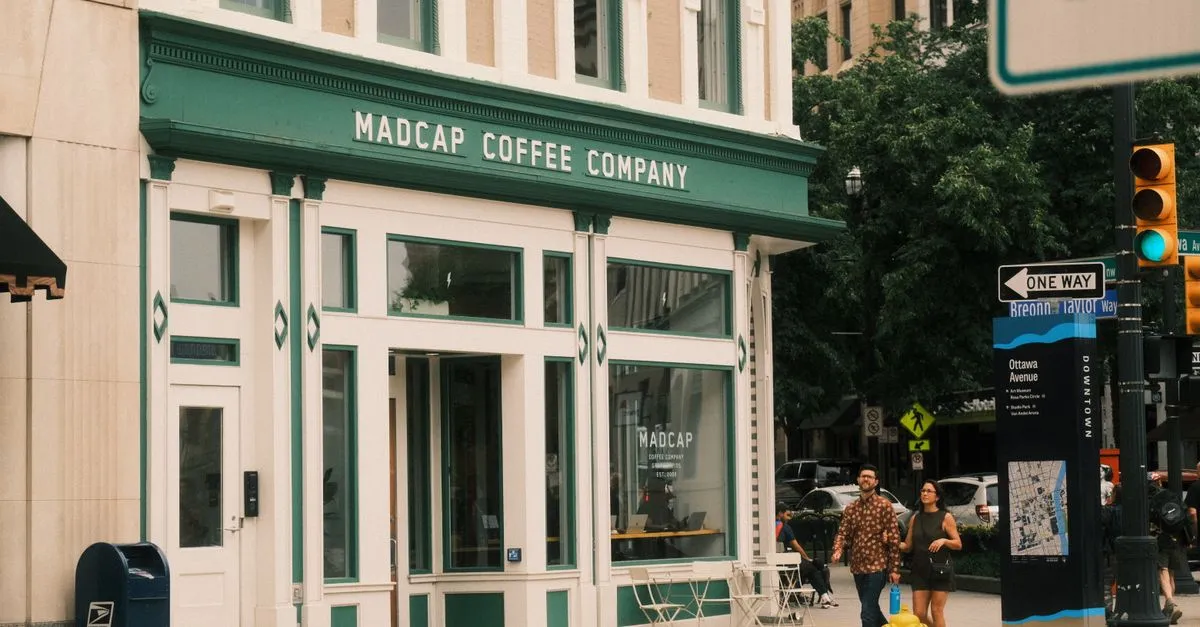 A couple walks past the Madcap Coffee Company storefront and a downtown wayfinding sign on Ottawa Avenue in Grand Rapids, Michigan.