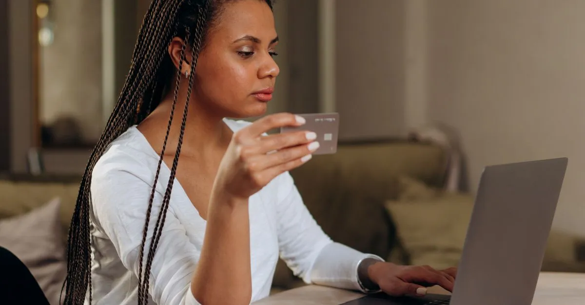 A woman holds a credit card while shopping on a laptop, completing an online purchase, the classic website conversion.