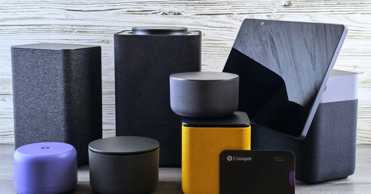 A collection of smart home speakers and a tablet display on a wooden surface, the kind of devices that answer voice searches.