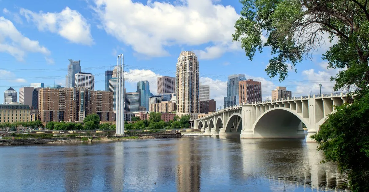 The Minneapolis skyline along the Mississippi River with the Third Avenue Bridge arching across the water.