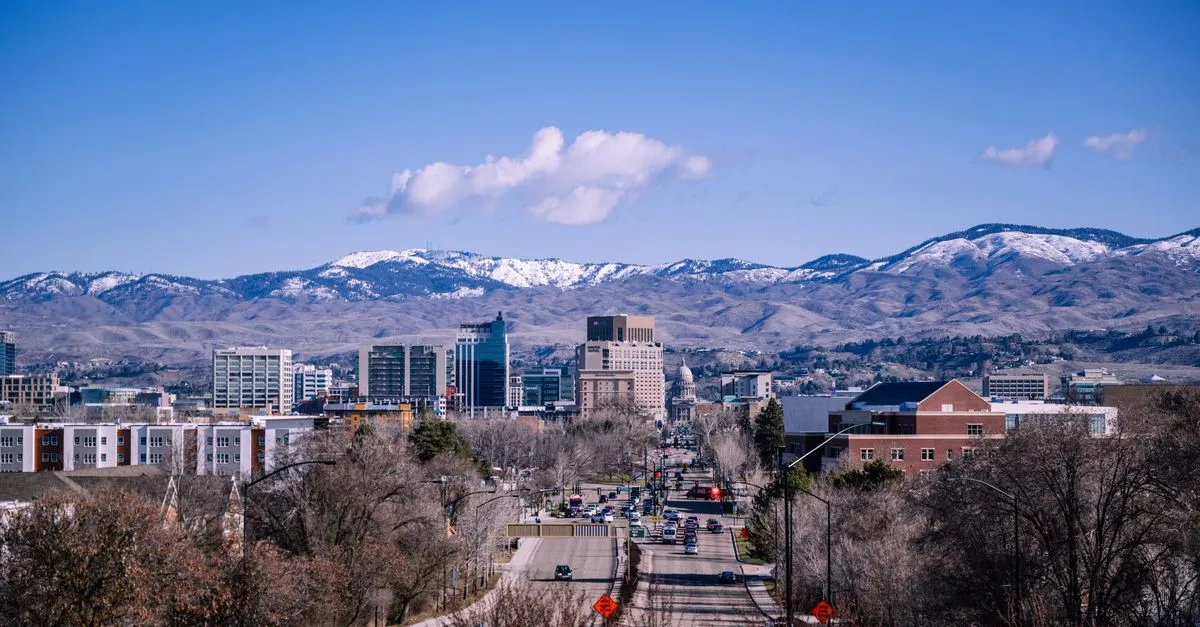 Downtown Boise, Idaho, with the Idaho State Capitol and mid-rise buildings sitting below the snow-dusted Boise Foothills under a clear blue sky.