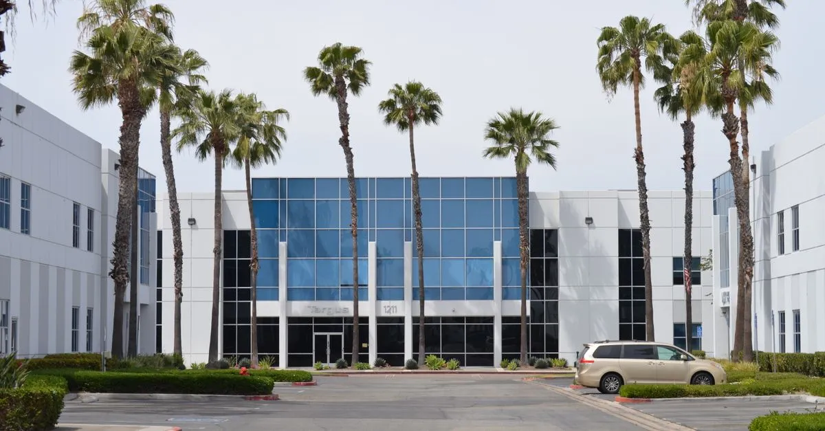 A modern two-story glass office building lined with tall palm trees in a Southern California office park.