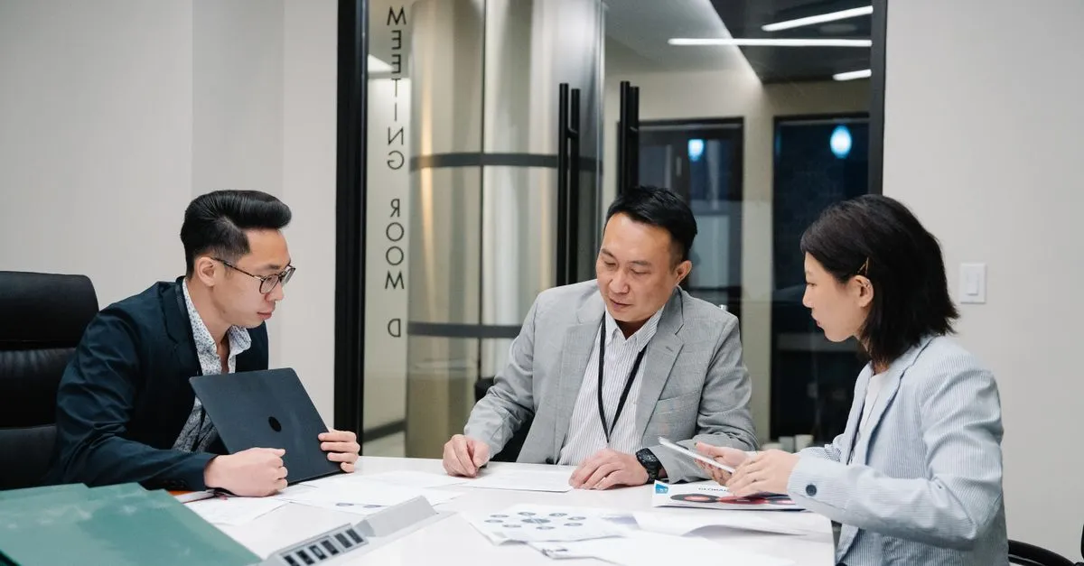 Three enterprise professionals reviewing analytics documents together in a corporate conference room.