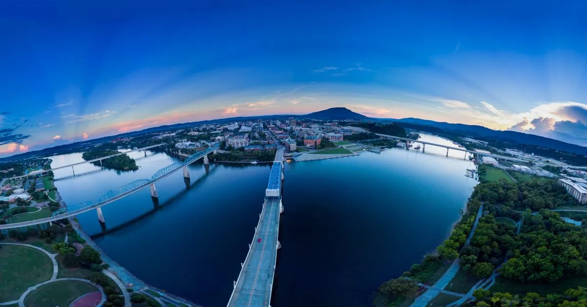 Aerial view of downtown Chattanooga, Tennessee at dusk with pedestrian and traffic bridges spanning the Tennessee River and Lookout Mountain in the distance.