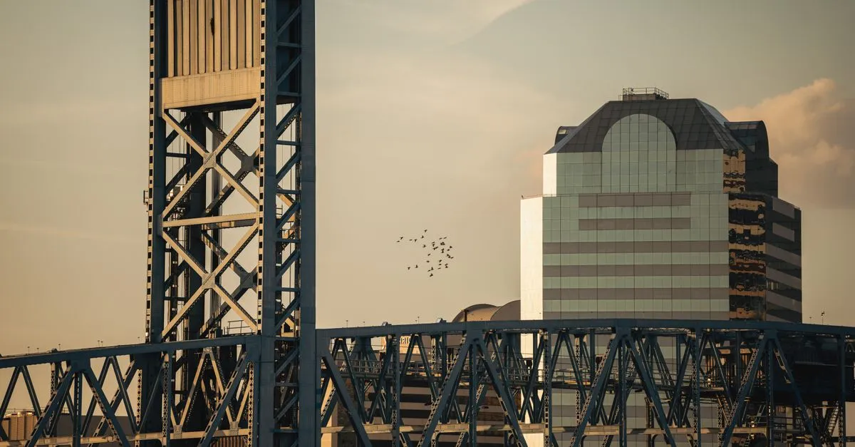 The Main Street Bridge crossing the St. Johns River at sunset, with a downtown Jacksonville office tower behind it.