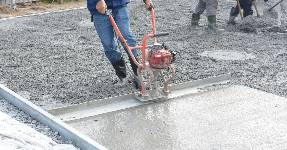 A concrete crew smoothing and leveling a freshly poured slab on a job site.