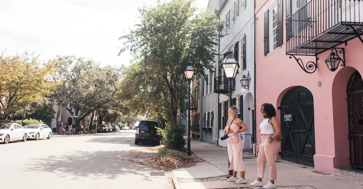 Two women stand on a historic Charleston street lined with pastel row houses and gas lanterns, the kind of walkable local market where near me searches happen.