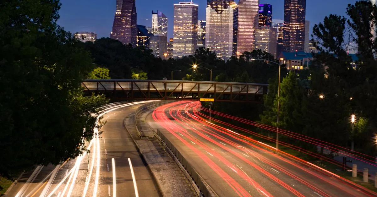 Long exposure of the Houston skyline at night with light trails from freeway traffic leading into the city.