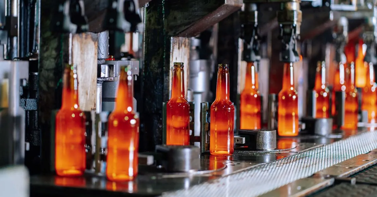 Amber glass bottles moving along an automated production line inside a glass factory.
