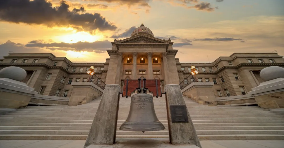The Idaho State Capitol in Boise at sunset, seen head-on from the front steps with the replica Liberty Bell in the foreground.