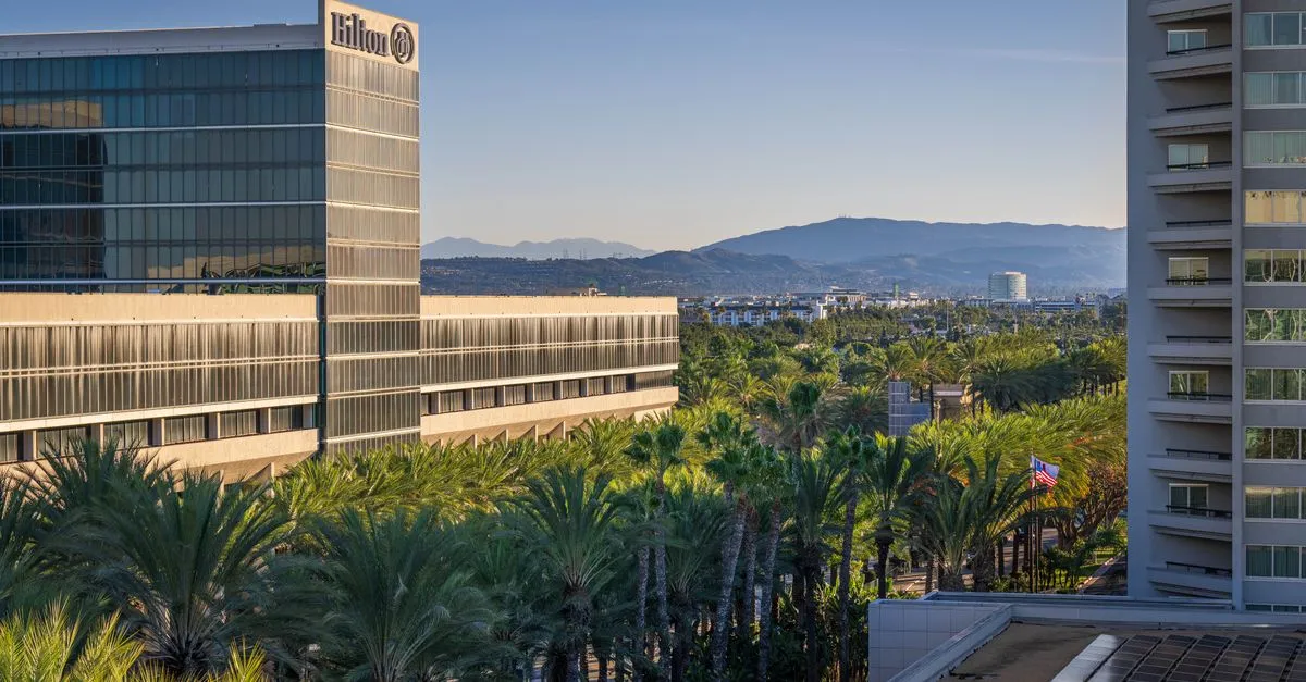 High-rise hotels above palm trees in the Anaheim Resort District at sunrise, with the Santa Ana Mountains in the distance.