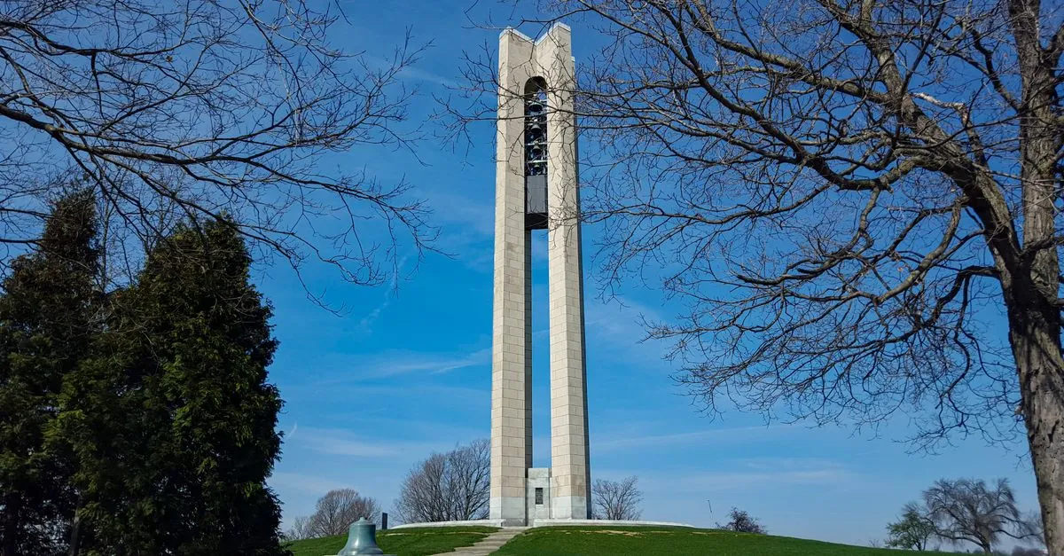 The Deeds Carillon bell tower at Carillon Historical Park in Dayton, Ohio, framed by bare trees under a blue sky.