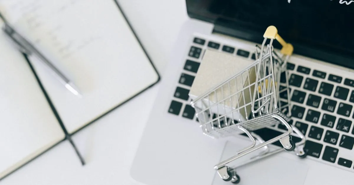 A miniature shopping cart sitting on a laptop keyboard, a nod to online shopping and AI-driven ecommerce.