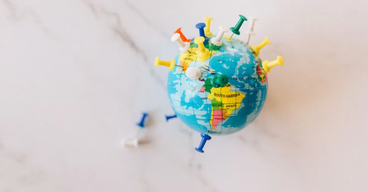 A small world globe studded with colorful push pins, resting on a white marble surface.