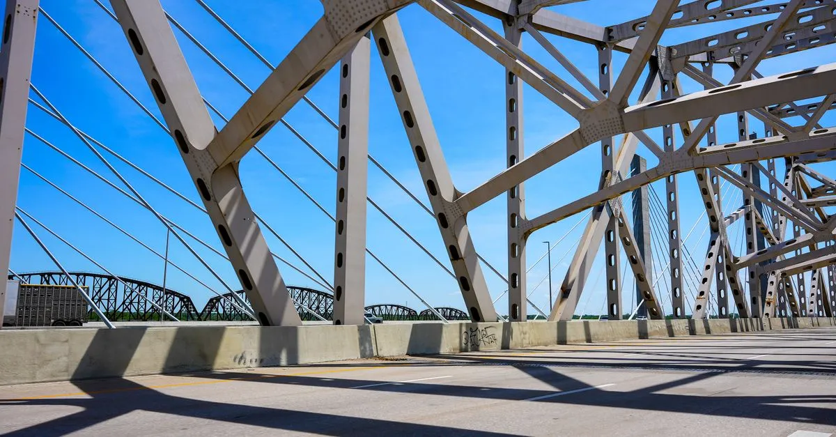 A steel truss bridge over the Ohio River in Louisville, Kentucky, under a clear blue sky, with a cable-stayed bridge visible in the distance.