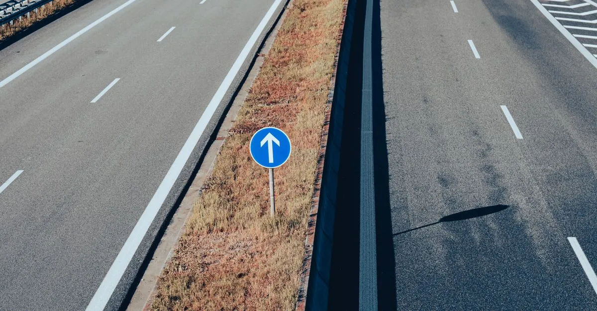 Aerial view of a highway with a blue arrow sign pointing straight ahead down the correct lane.